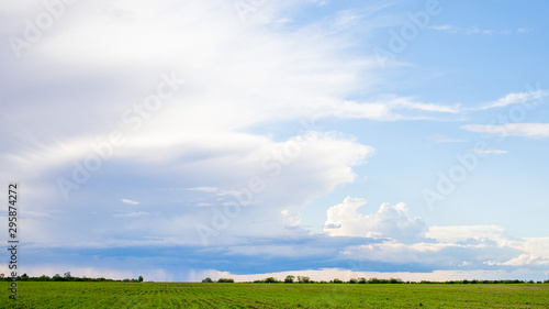 Dark clouds on sky with one part with rain over agricultural fields in distance