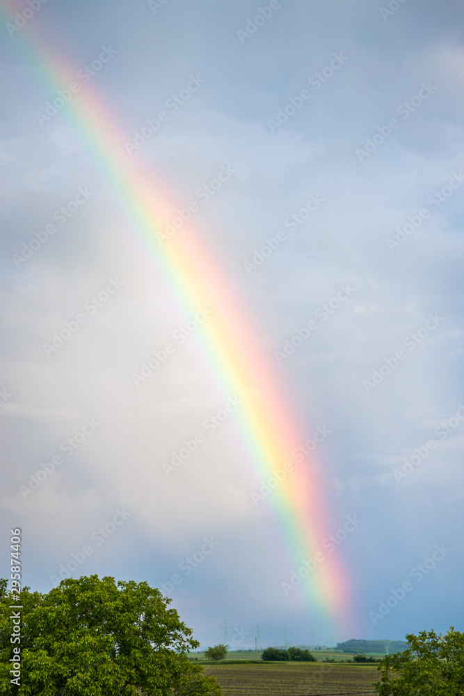 Rainbow over trees and agricultural fields with cloudy sky in background Rainbow over trees and agricultural fields with cloudy sky in background