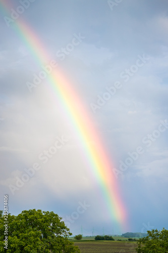 Rainbow over trees and agricultural fields with cloudy sky in background