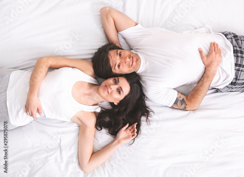 Top view of young happy millennial couple lying in bed