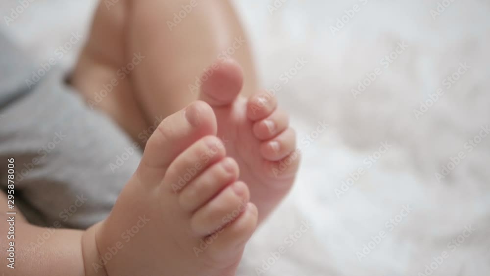 Beautiful cute little baby legs are touching each other. Child is on white bedspread. Close-up Beautiful cute little baby legs are touching each other. Child is on white bedspread. Close-up