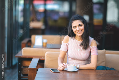 Young woman with smartphone holding cup coffee in a cafe