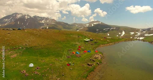 A following 4k helshot from some tourists base camp deep in nature Some people attending in camp near a lagoon melted snows in mountains and clouds dancing in the sky perfect colorful landscape 