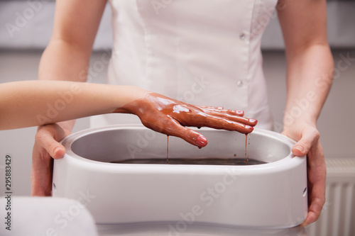Fotografia Female hand in beauty spa  salon with paraffin wax in bowl held by beautician therapist