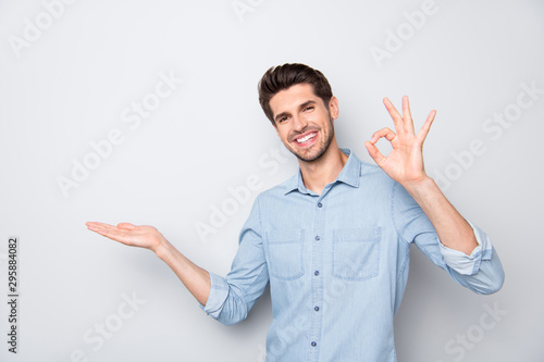 Portrait of positive cheerful promoter man hold hand demonstrate adverts present feedback recommend perfect novelty show ok sign wear casual style clothes isolated over grey color background