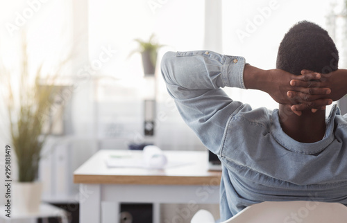 Black worker sitting in office with hands behind his head