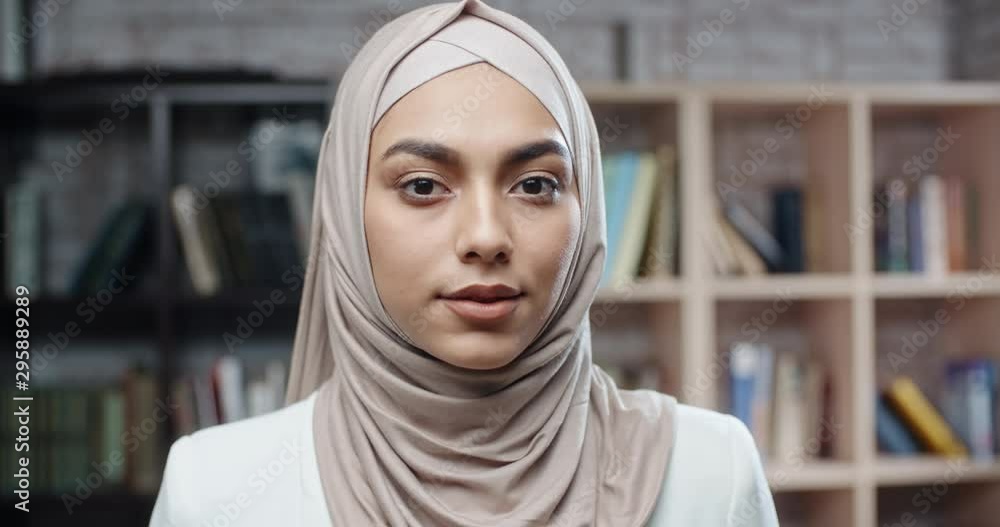 Female muslim student in library, holding books and looking at camera, girl wearing hijab spending time studying - modern islam, student lifestyle concept close up 4k Female muslim student in library, holding books and looking at camera, girl wearing hijab spending time studying - modern islam, student lifestyle concept close up 4k
