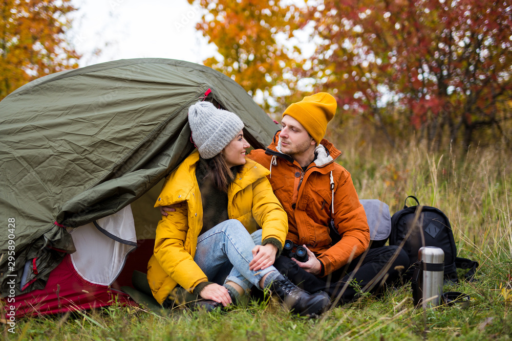 trekking and hiking concept - portrait of cute couple sitting near green tent in autumn forest