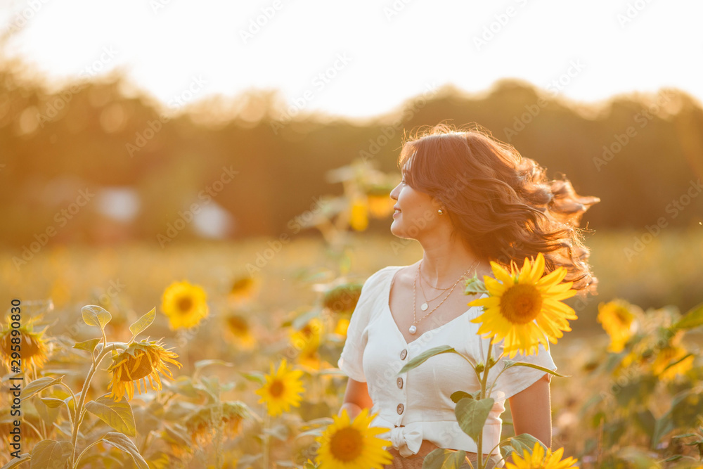 Young Asian woman with curly hair in a field of sunflowers at sunset ...