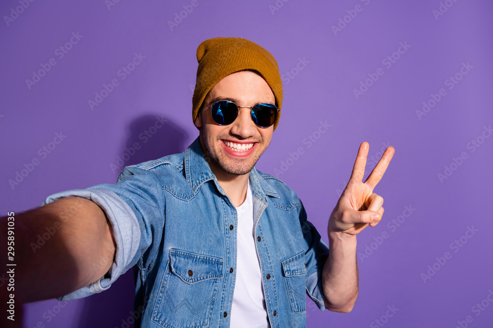 Self portrait of trendy cheerful kind stylish attractive handsome guy taking selfie showing you v-sign smiling toothily isolated over vivid purple color background