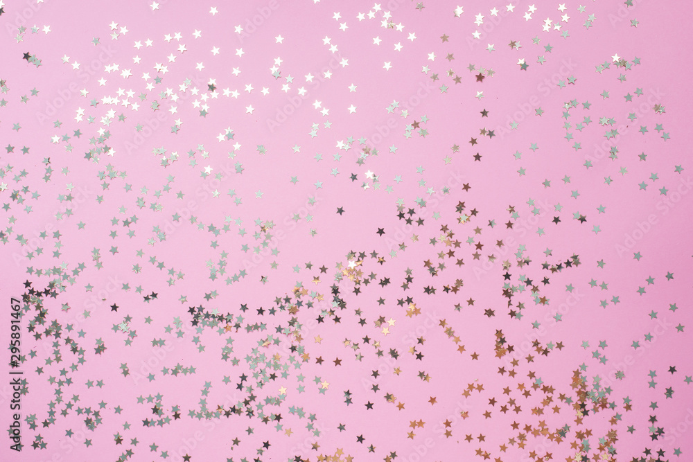 Confetti of gold stars glisten on a pink background. Festive holiday pastel backdrop.