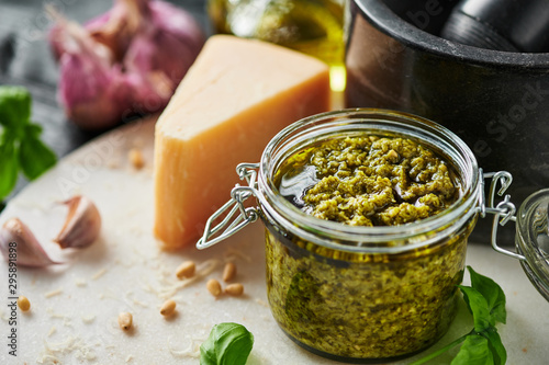 Pesto sauce or pesto genovese in a glass jar with pine nuts, parmesan, basil, oil and garlic on white marble cutting board. Copy space. photo
