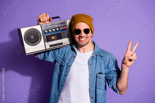 Photo of confident cheerful kind friendly man showing you v-sign smiling toothily holding retro recorder with hands wearing white t-shirt isolated over purple vibrant color background
