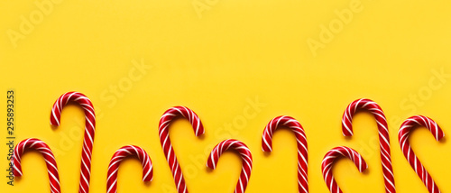 Banner with Christmas candy cones on yellow background. Colorful holiday sweets with bright copy space. Traditional dessert wtih red and white stripes.
