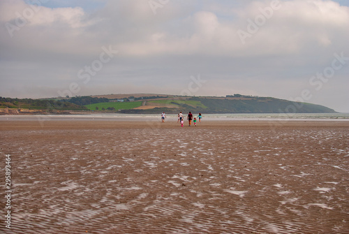 People walking on sandy beach. Family with children and a dog walking and playing on Kilbrittain beach, Ireland. enjoying the day. Cloudy day.
