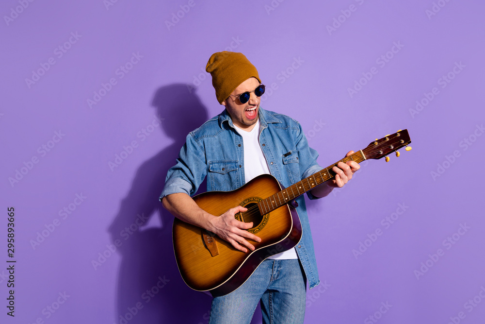 Obraz premium Photo of cheerful rude attractive handsome man wearing cap holding guitar with hands playing musician instrument wearing spectacles isolated over purple vivid color background