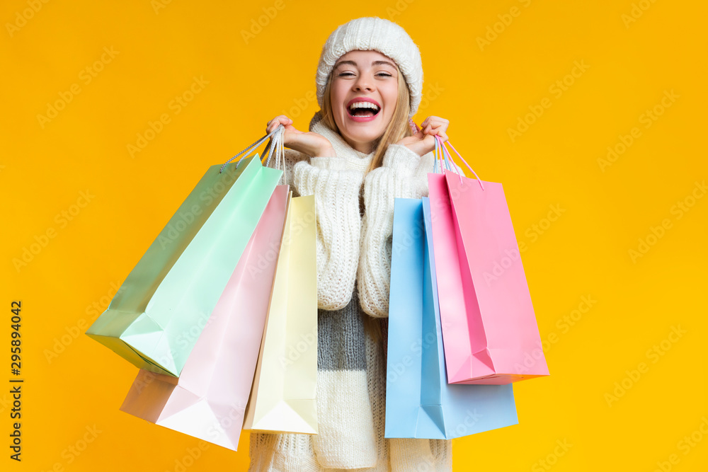 Overjoyed blonde girl in white hat with shopping bags