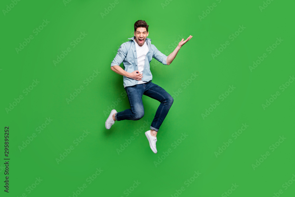 Full length body size photo of cheerful positive ecstatic overjoyed man pretending to be playing guitar wearing white sneakers jumping like rocker on stage isolated over green vivid color background