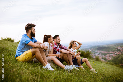 Group of young friends sitting on the on the grass at a hill and drinking cider