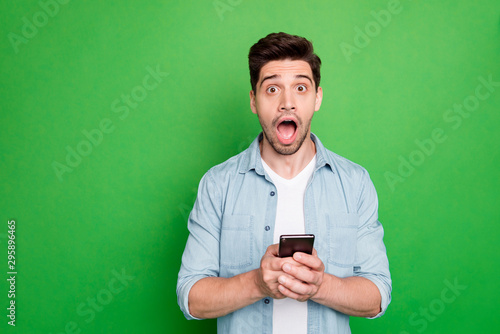 Photo of amazing guy holding telephone read instagram post negative comments not believe eyes open mouth wear denim shirt isolated green color background