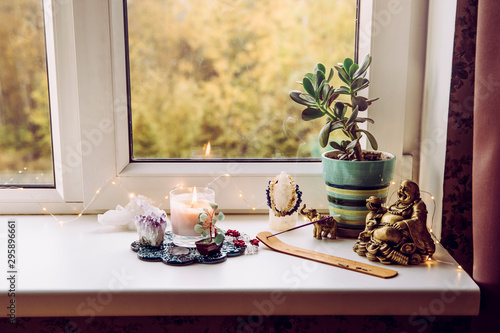 Asian money tree Crassula Ovata growing on window sill in home Feng Shui wealth and prosperity invitation altar. With smoking incense stick, laughing golden Buddha and crystal clusters. 