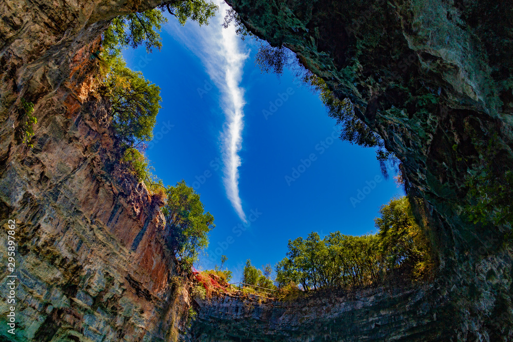 View of the clear blue sky with light clouds. Sql the failure of the ceiling of the underground cave