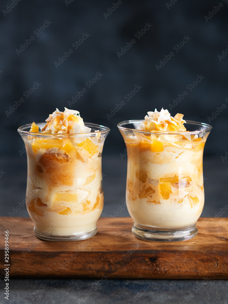 Pineapple, peach, Coconut Trifle dessert mouse in a glass on a dark background with copy space. Vegan recipe dessert concept. Selective focus. Pineapple, peach, Coconut Trifle dessert mouse in a glass on a dark background with copy space. Vegan recipe dessert concept. Selective focus.