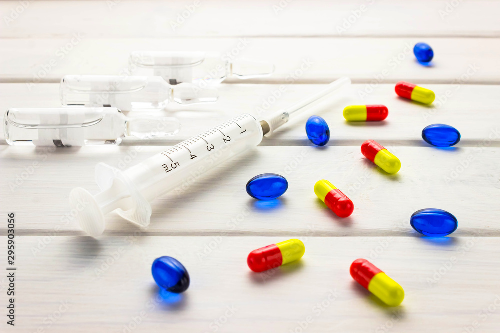 Prevention of influenza. The vaccine syringe and the bright capsules pills on a wooden white background. The concept of medicine and the industry of medicines Prevention of influenza. The vaccine syringe and the bright capsules pills on a wooden white background. The concept of medicine and the industry of medicines