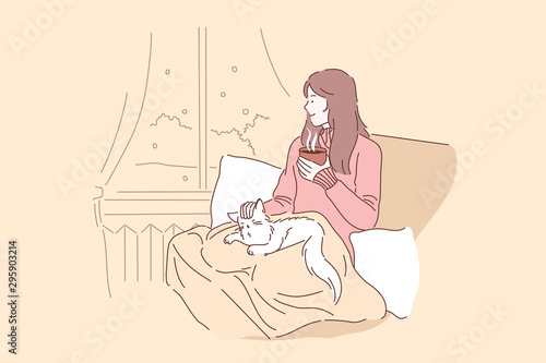 Cozy, relax, dream concept. Young woman or girl enjoys the comfort of sitting on a chair with a blanket and caressing her pet cat. Thoughtful lady in looks out the window and drinks tea or coffee.