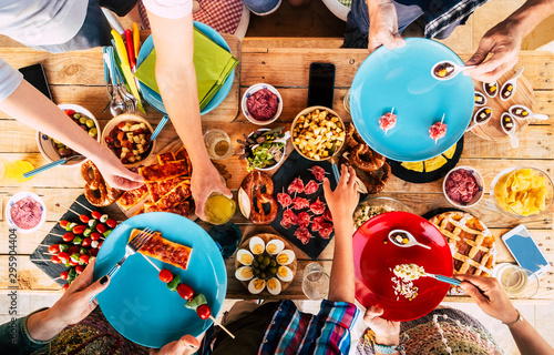 Coloured and mixed food table with people friends taking and eat together in friendship - celebration time and leisure activity at home or restaurant - wooden table background