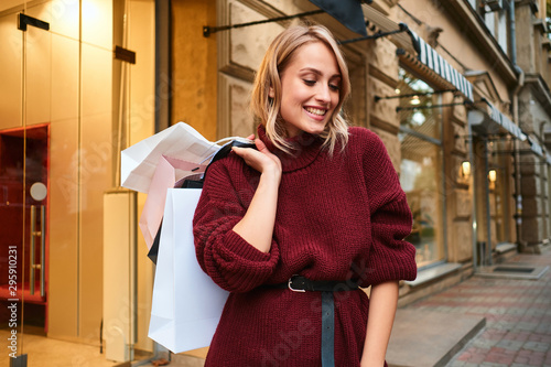 Attractive happy blond girl in knitted sweater with shopping bags after shopping on street