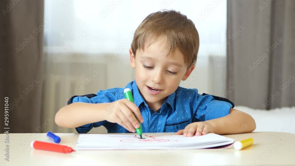 A cute boy sits at a table in a room and spends time painting with colored felt pen. A cute boy sits at a table in a room and spends time painting with colored felt pen.