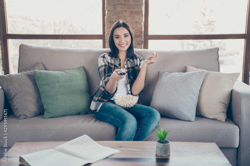 Obraz premium Photo of amazing lady going to watch favorite humor tv show holding remote controller and popcorn plate sitting sofa wearing casual clothes apartment indoors