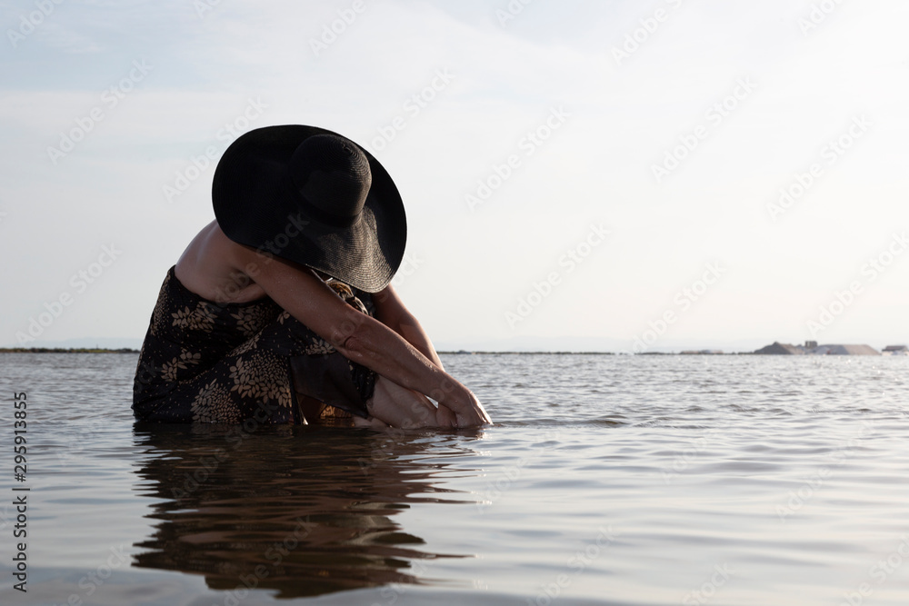 Mujer triste con sombrero ancho sentada dentro del agua de la playa Stock  Photo | Adobe Stock