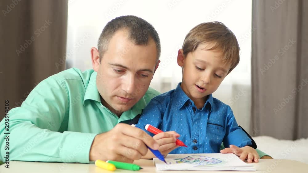 Portrait of a happy family. Father and son draw with colored markers, sitting at the table. Portrait of a happy family. Father and son draw with colored markers, sitting at the table.