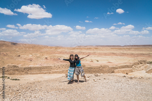 Two caucasian european white traveler girls standing on top of a cliff spreading arms over a desert land in Morocco
