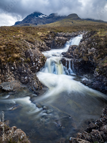 A small waterfall in a river with the Cuilin mountains in the background