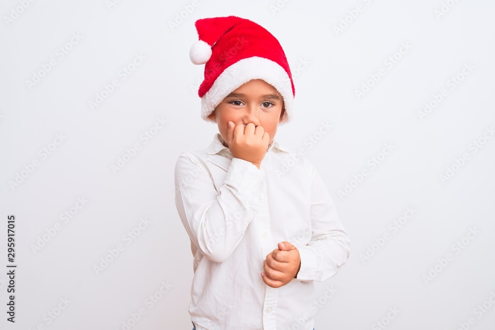 Beautiful kid boy wearing Christmas Santa hat standing over isolated white background looking stressed and nervous with hands on mouth biting nails. Anxiety problem.