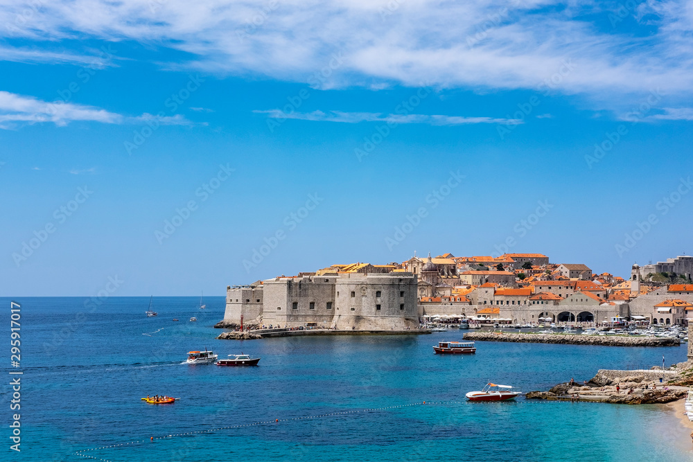 Old city walls in historic Dubrovnik city, Dalmatia, Croatia, emerald Adriatic Sea with boats and blue summer sky, popular touristic destination