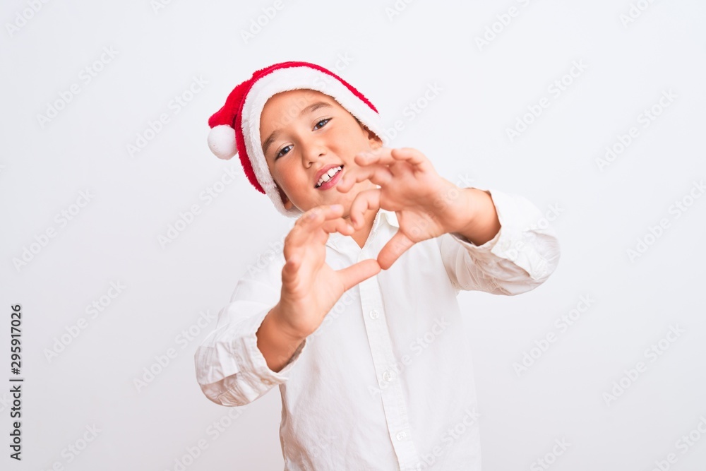 Beautiful kid boy wearing Christmas Santa hat standing over isolated white background smiling in love doing heart symbol shape with hands. Romantic concept. Beautiful kid boy wearing Christmas Santa hat standing over isolated white background smiling in love doing heart symbol shape with hands. Romantic concept.