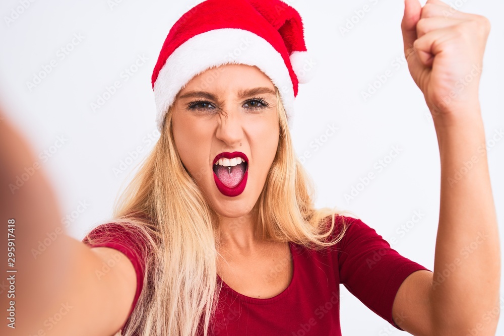 Woman wearing Christmas Santa hat make selfie by camera over isolated white background annoyed and frustrated shouting with anger, crazy and yelling with raised hand, anger concept Woman wearing Christmas Santa hat make selfie by camera over isolated white background annoyed and frustrated shouting with anger, crazy and yelling with raised hand, anger concept