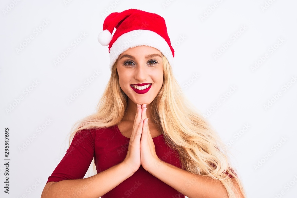 Young beautiful woman wearing Christmas Santa hat over isolated white background praying with hands together asking for forgiveness smiling confident. Young beautiful woman wearing Christmas Santa hat over isolated white background praying with hands together asking for forgiveness smiling confident.