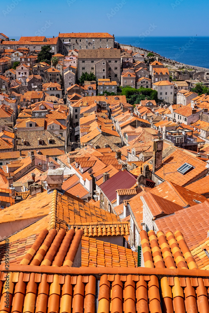 Sone houses with red roofs in old historic Dubrovnik city, stone city walls in background on sunny summer day and blue Adriatic Sea, Dalmatia, Croatia, the most popular touristic destination