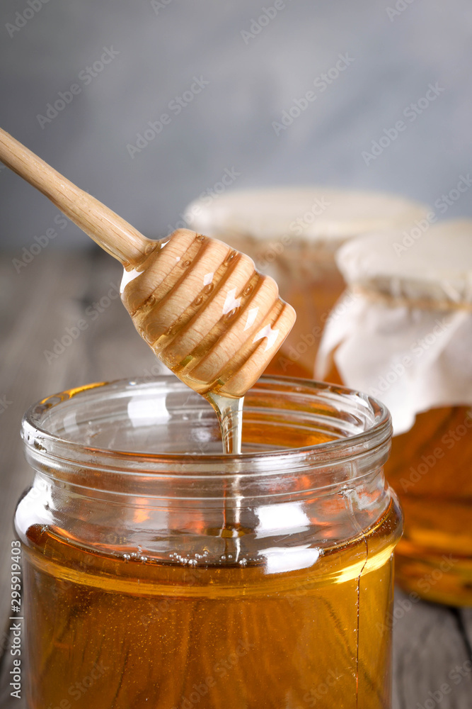 Pouring aromatic honey into jar, closeup. Honey in glass jars and honeycombs wax on wooden background. Wooden stick , instruments Pouring aromatic honey into jar, closeup. Honey in glass jars and honeycombs wax on wooden background. Wooden stick , instruments