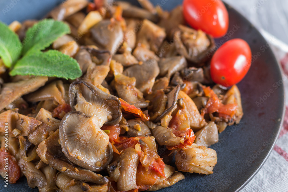 Fried oyster mushrooms with tomatoes on gray concrete background. side view. Fried oyster mushrooms with tomatoes on gray concrete background. side view.