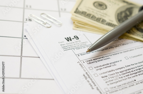 IRS Form W-9 Request for taxpayer identification number and certification blank lies with pen and many hundred dollar bills on calendar page photo