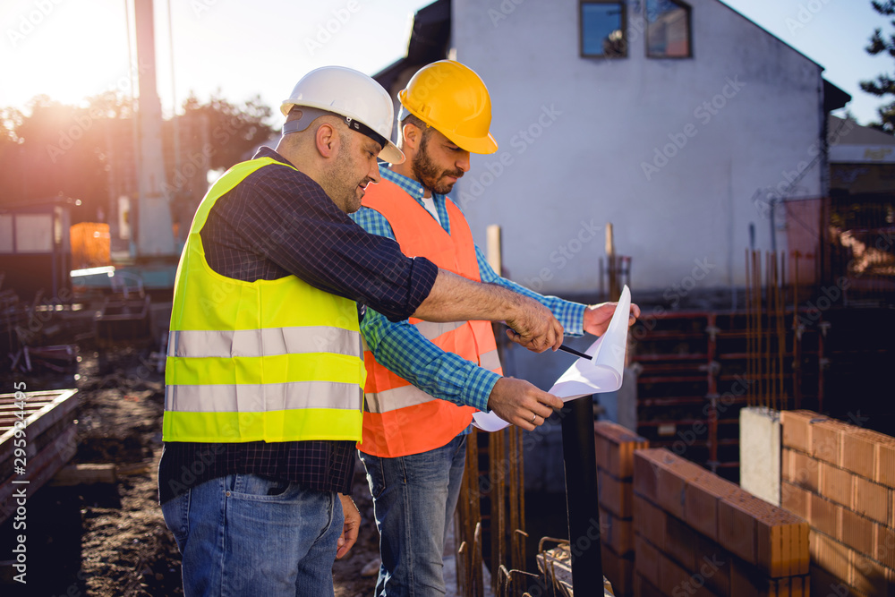 Men in hardhat and yellow and orange jacket posing on building site. stock photo Men in hardhat and yellow and orange jacket posing on building site. stock photo
