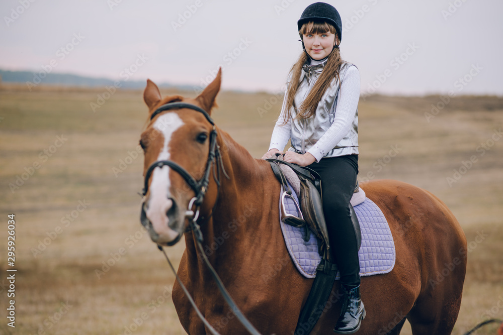 Obraz premium First lessons of horseback riding. Young beautiful girl riding a horse in a field.