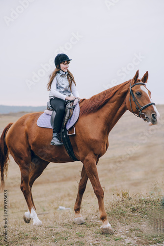 First lessons of horseback riding. Young beautiful girl riding a horse in a field.