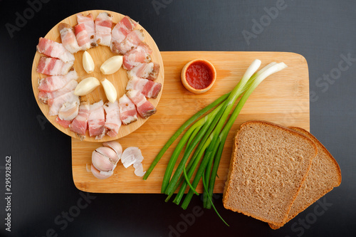 BACON WITH BREAD ONIONS AND KETCHUP ON A WOODEN BOARD ON A BLACK TABLE. Flatley photo